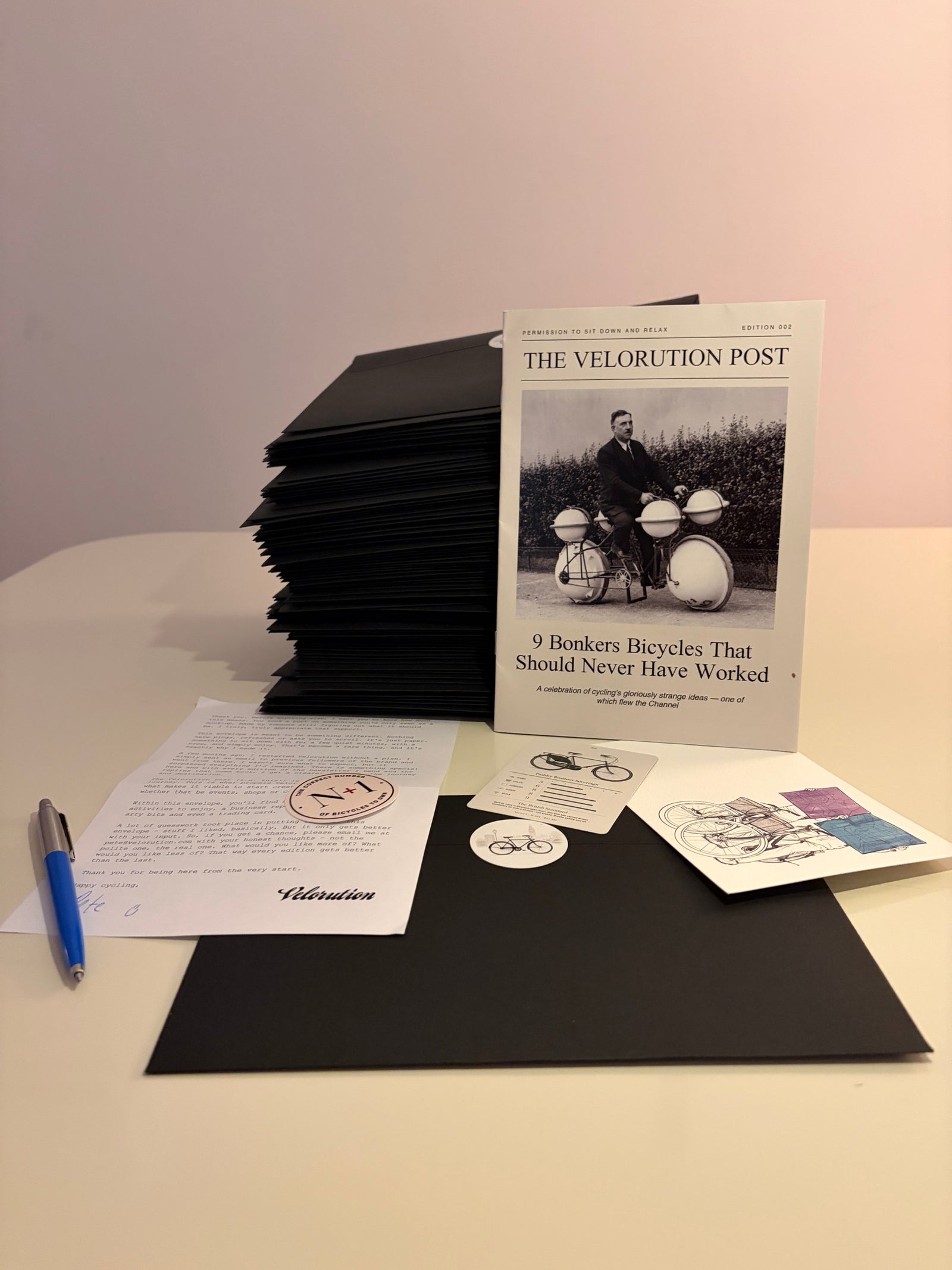 The Velorution Post monthly envelope contents — mini magazine, personal letter, collectable trading card, stickers and artwork
