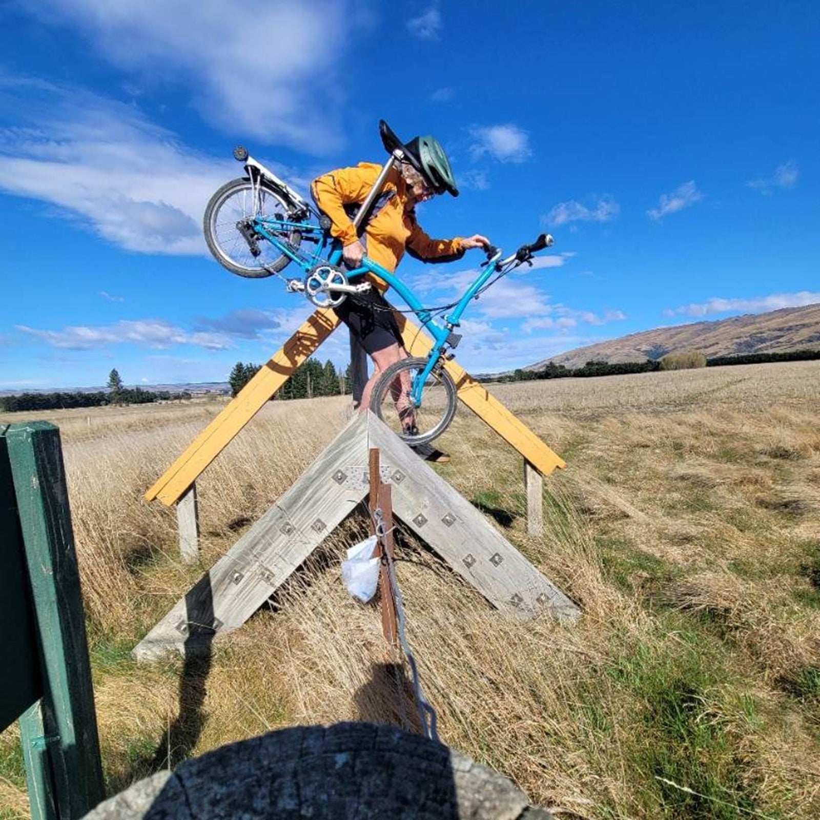 Annemarie Jutel lifting her folding Brompton over a wooden stile on a New Zealand cycle trail
