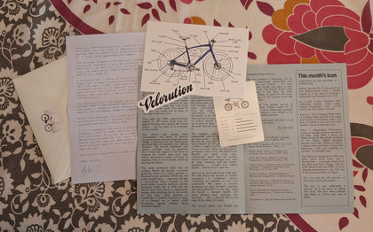 The contents of The Velorution Post laid out on a table — letter, article, trading card and postcard